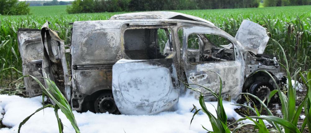 Ein ausgebranntes Auto steht in einem Feld, umgeben von Löschschaum. In dem Auto ist eine Leiche entdeckt worden.