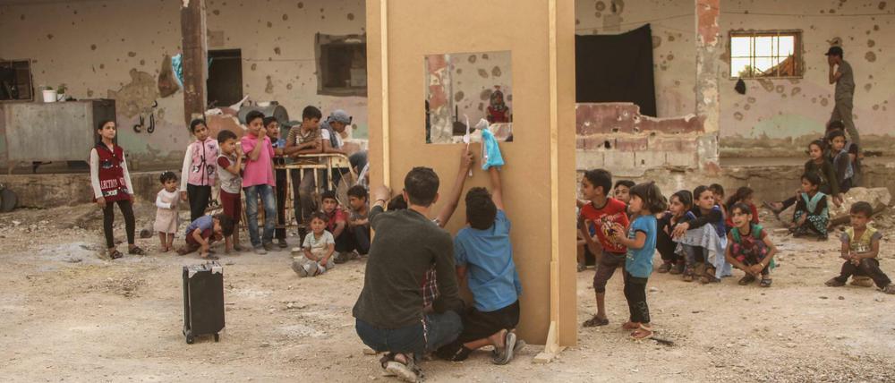 Ein Puppenspiel vor einer zerstörten Schule in Syrien, die vertrieben Kindern als Unterkunft dient.