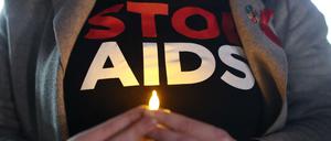 Eine Person hält ein künstliches Teelicht vor dem Körper, auf ihrem T-Shirt ist "Stop Aids" zu lesen.