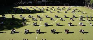 In Dreiergruppen versammeln sich Berliner Abiturienten im Juni 2020 zur Zeugnisübergabe auf einem Sportplatz.