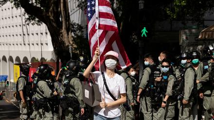 Sympathy with the devil. Hongkonger Polizisten in voller Montur hinter einer Frau, die anlässlich des US-Unabhängigkeitstages eine Flagge der USA vor dem US-Konsulat schwenkt. Am 2. Juli erteilte der US-Senat seine endgültige Zustimmung zum "Hong Kong Autonomy Act" der die Verhängung von Sanktionen gegen chinesische Einzelpersonen und Banken vorsieht, die die Autonomie Hongkongs untergraben. 