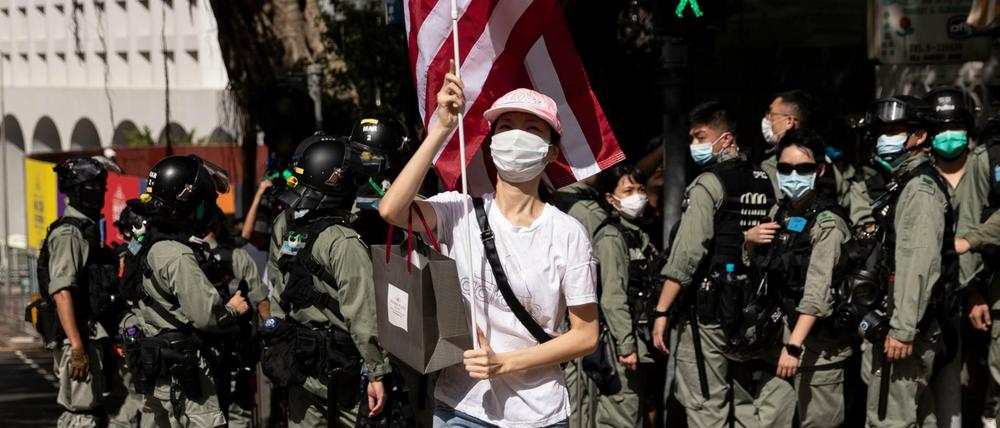 Sympathy with the devil. Hongkonger Polizisten in voller Montur hinter einer Frau, die anlässlich des US-Unabhängigkeitstages eine Flagge der USA vor dem US-Konsulat schwenkt. Am 2. Juli erteilte der US-Senat seine endgültige Zustimmung zum "Hong Kong Autonomy Act" der die Verhängung von Sanktionen gegen chinesische Einzelpersonen und Banken vorsieht, die die Autonomie Hongkongs untergraben.