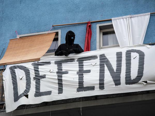 Ein vermummter Mann steht auf einem Balkon eines Hauses im Friedrichshainer Nordkiez.