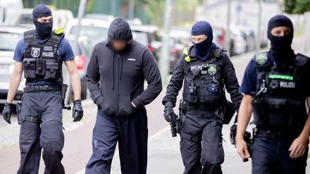 Ein Mann wird bei einer Razzia in Gesundbrunnen von Beamten zu einem Polizeiwagen begleitet. 