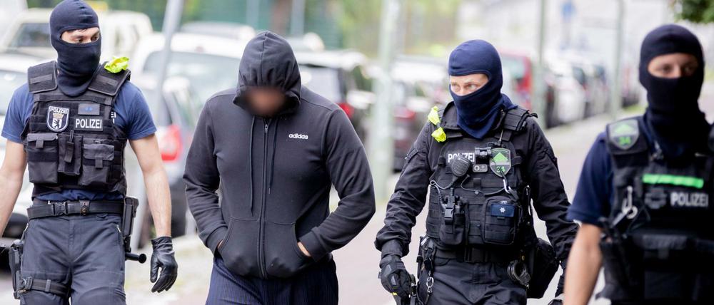 Ein Mann wird bei einer Razzia in Gesundbrunnen von Beamten zu einem Polizeiwagen begleitet.