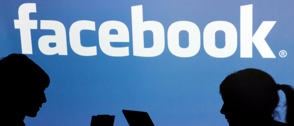 Die Schatten von Jugendlichen mit einem Laptop sind vor dem Schriftzug des sozialen Internet-Netzwerks Facebook zu sehen.