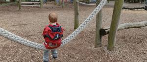 Ein fünfjähriger Junge sitzt allein auf einer Schaukel auf einem Abenteuerspielplatz in Berlin.