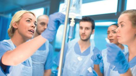 Krankenpflegepersonal steht um eine Kollegin herum, die anhand eines Tropfes Erläuterungen abgibt.