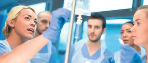 Krankenpflegepersonal steht um eine Kollegin herum, die anhand eines Tropfes Erläuterungen abgibt.