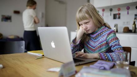 Ein Mädchen sitzt zu Hause am Küchentisch am Laptop.
