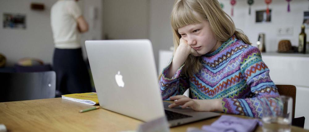 Ein Mädchen sitzt zu Hause am Küchentisch am Laptop.