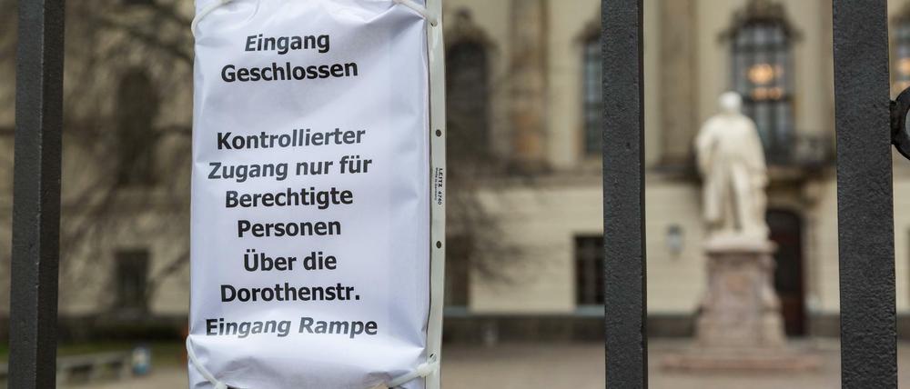 Zettel am Zaun vor dem Hauptgebäude der Humboldt-Universität, der Zugangsberechtigte auf einen Hintereingang verweist.
