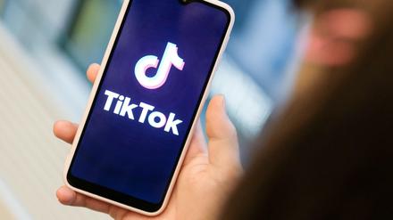 Ein Mädchen hält ihr Smartphone in den Händen, auf dem sie ein Foto der Kurzvideo-App Tiktok geöffnet hat.