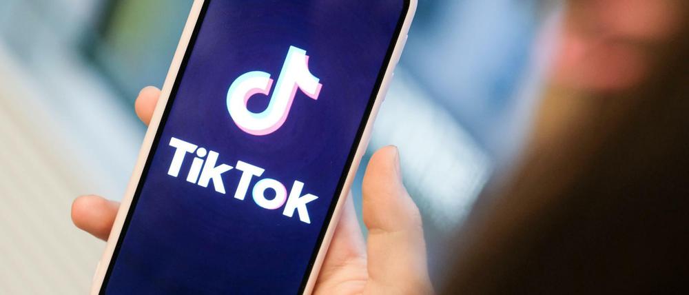 Ein Mädchen hält ihr Smartphone in den Händen, auf dem sie ein Foto der Kurzvideo-App Tiktok geöffnet hat.