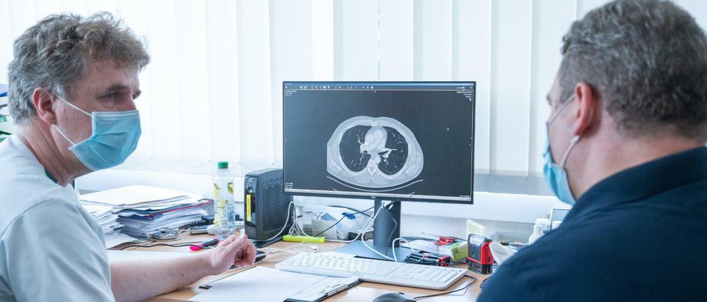 Der Lungenfacharzt Torsten Blum (l.) erklärt einem Covid-19-Patienten auf einer Computertomographie die Spuren, die Covid-19 in der Lunge hinterlassen hat.