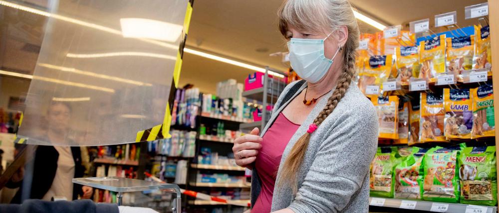Eine Supermarktkundin mit Alltagsmaske beim Bezahlen an der Kasse. Die Kassiererin ist mit einer Scheibe geschützt und trägt Handschuhe.