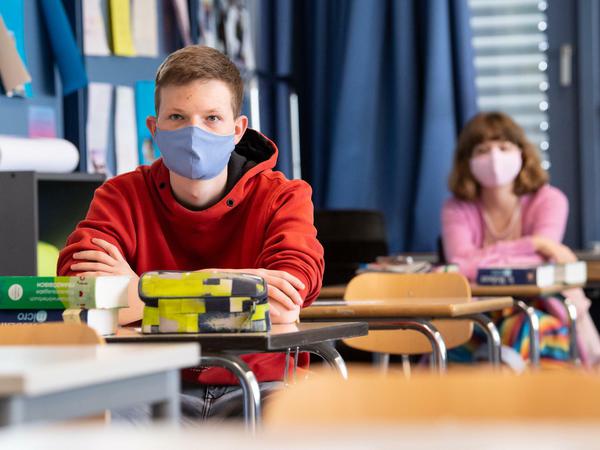 Ein Schüler und eine Schülerin einer höheren Klasse sitzen mit Masken im Unterricht.