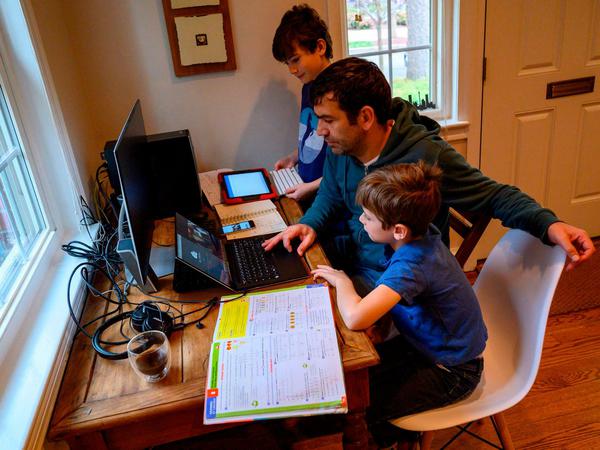 Ein Vater unterstützt seine beiden Söhne beim Homeschooling.