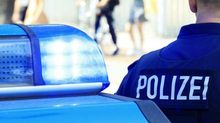 Symbolbild: Die Blaulichter eines Polizeiautos im Einsatz leuchten. Daneben steht ein Polizist.