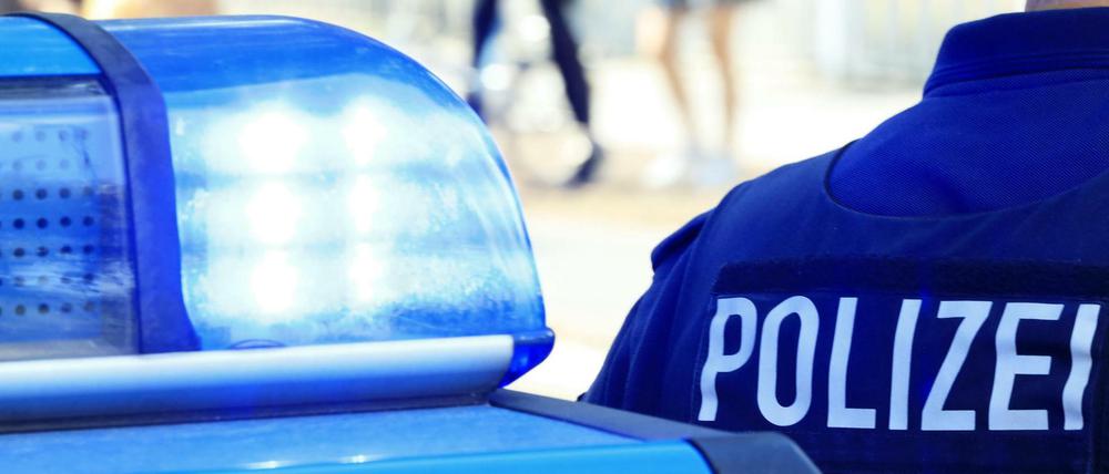 Symbolbild: Die Blaulichter eines Polizeiautos im Einsatz leuchten. Daneben steht ein Polizist.