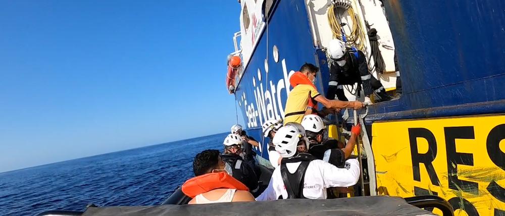 Migranten und Sea-Watch-Mitarbeiterinnen klettern an Bord. 