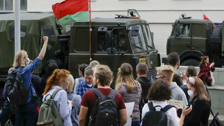 Demonstranten in Minsk stehen vor Polizeifahrzeugen.