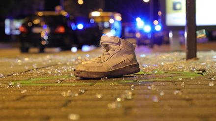 Ein einzelner Sportschuh liegt nach dem Verkehrsunfall an einer Bushaltestelle zwischen Glasscherben in einem Farbkreis der Spurensicherung der Polizei. 