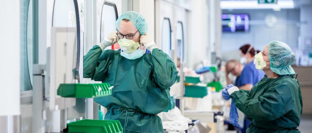Vor einem Krankenzimmer auf einer Intensivstation bekleiden sich zwei Pflegepersonen mit Schutzkleidung.