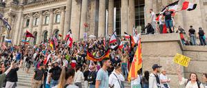 Teilnehmer einer Kundgebung gegen die Corona-Maßnahmen stehen auf den Stufen zum Reichstagsgebäude, zahlreiche Reichsflaggen sind zu sehen. 