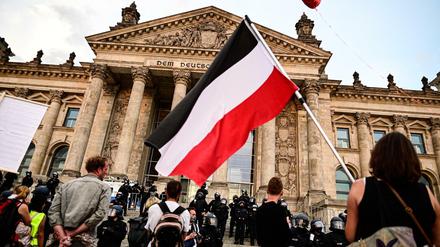 Teilnehmer einer Kundgebung gegen die Corona-Maßnahmen stehen vor dem Reichstag, ein Teilnehmer hält eine Reichsflagge.