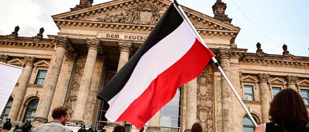 Teilnehmer einer Kundgebung gegen die Corona-Maßnahmen stehen vor dem Reichstag, ein Teilnehmer hält eine Reichsflagge.