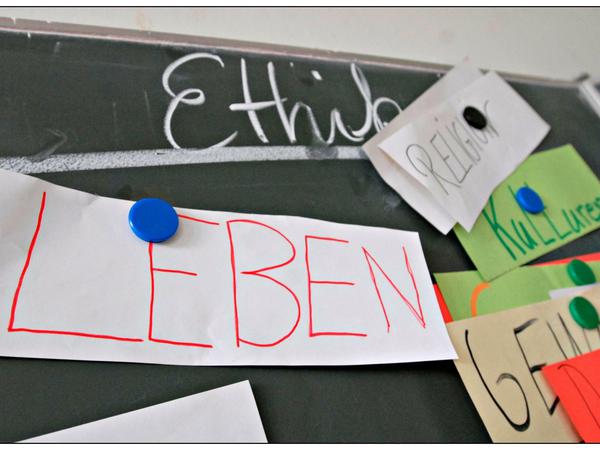 An einer Tafel steht mit weißer Kreise das Wort Ethik, mit Magneten angepinnt sind Zettel mit Begriffen wie Leben, Religion, Kulturen.