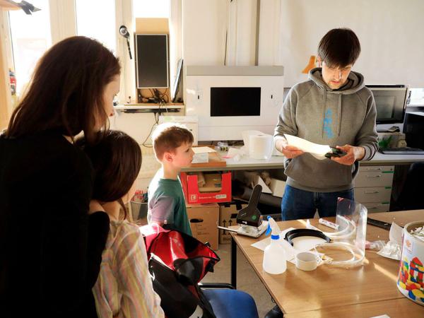 Ein Blick in die Werkstatt des Potsdamer Wissenschaftsladen, in dem eine Familie beim Bau von Gesichtsschildern zuguckt.