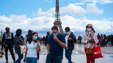 Passanten tragen am Platz Trocadero in der Nähe des Eiffelturms Mundschutze und Gesichtsmasken.