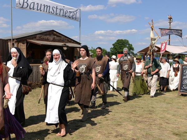 Verkleidete Personen gehen in einer Prozession über einen Festplatz.