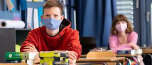 Ein Schüler und eine Schülerin sitzen in einem Klassenraum an Einzeltischen und tragen Mund-Nasen-Schutz.