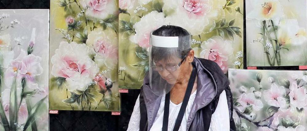 Eine Frau sitzt in Kiew mit einem Gesichtsschild neben gemalten Bildern. 
