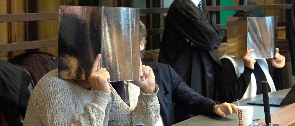 Zwei der Angeklagten sitzen neben ihren Anwälten im Gerichtssaal und verdecken ihre Gesichter.