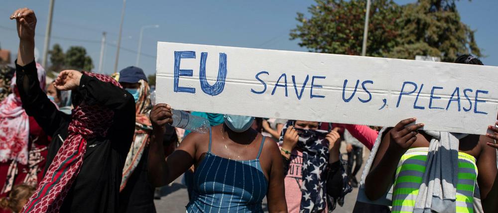 Migrantinnen und Migranten auf Lesbos rufen bei einem Protest Parolen und halten ein Schild mit der Aufschrift: EU, rette uns bitte. 
