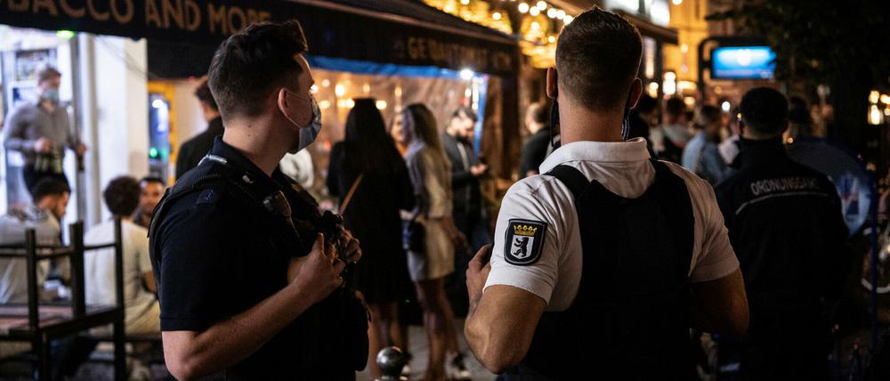 Ein Polizeibeamter und ein Mitarbeiter des Ordnungsamtes stehen vor einem Lokal in Mitte.