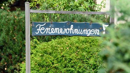 Ein Schild "Ferienwohnungen!" steht vor einem Haus zwischen Bäumen und Sträuchern. 