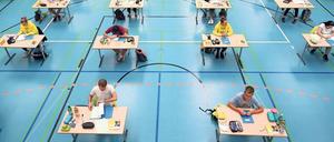 In einer Turnhalle sitzen Abiturienten und Abiturientinnen an Einzeltischen.