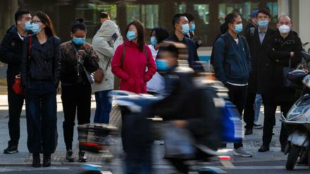 Menschen in China tragen Schutzmasken und warten während des morgendlichen Berufsverkehrs darauf, eine Straße zu überqueren. (Symbolbild)