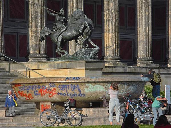 Eine monumentale Granitschale, die mit Graffitos beschmiert ist, wird von Jugendlichen fotografiert.