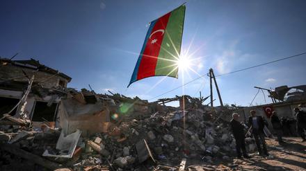 Die Fahne von Aserbaidschan weht am 22.10.2020 über zerstörten Häusern in einem Wohngebiet nahe der Grenze zu Armenien, welches über Nacht von armenischen Truppen mit Raketen beschossen wurde. 
