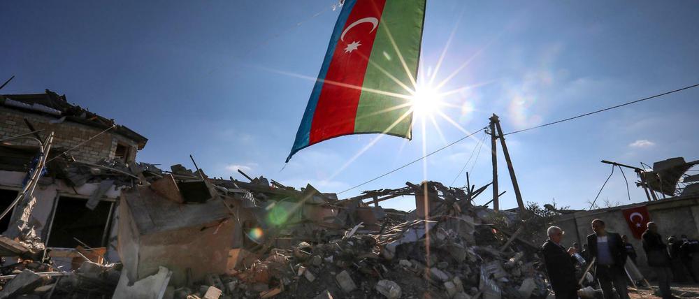 Die Fahne von Aserbaidschan weht am 22.10.2020 über zerstörten Häusern in einem Wohngebiet nahe der Grenze zu Armenien, welches über Nacht von armenischen Truppen mit Raketen beschossen wurde.