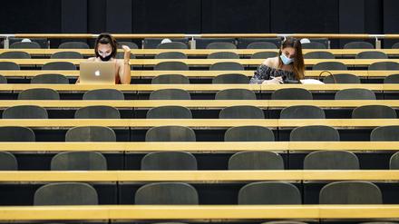 Zwei Studentinnen sitzen mit Mund-Nasen-Schutz in einem fast leeren Hörsaal.