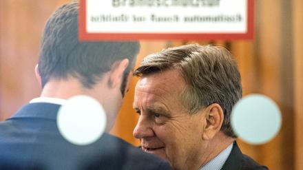 Ex-BER-Chef Hartmut Mehdorn unterhält sich hinter einer Glastür auf der Sitzung der Fluglärmkommission in Schönefeld (Brandenburg).