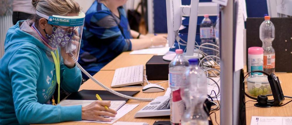 Mitarbeiter des Gesundheitsamtes Mitte mit Gesichtsschutzschirm telefonieren im Lagezentrum des Gesundheitsamt Mitte. 