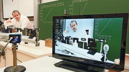 Ein Professor ist bei einer Physik-Vorlesung im Hörsaal live und auf einem Bildschirm zu sehen.
